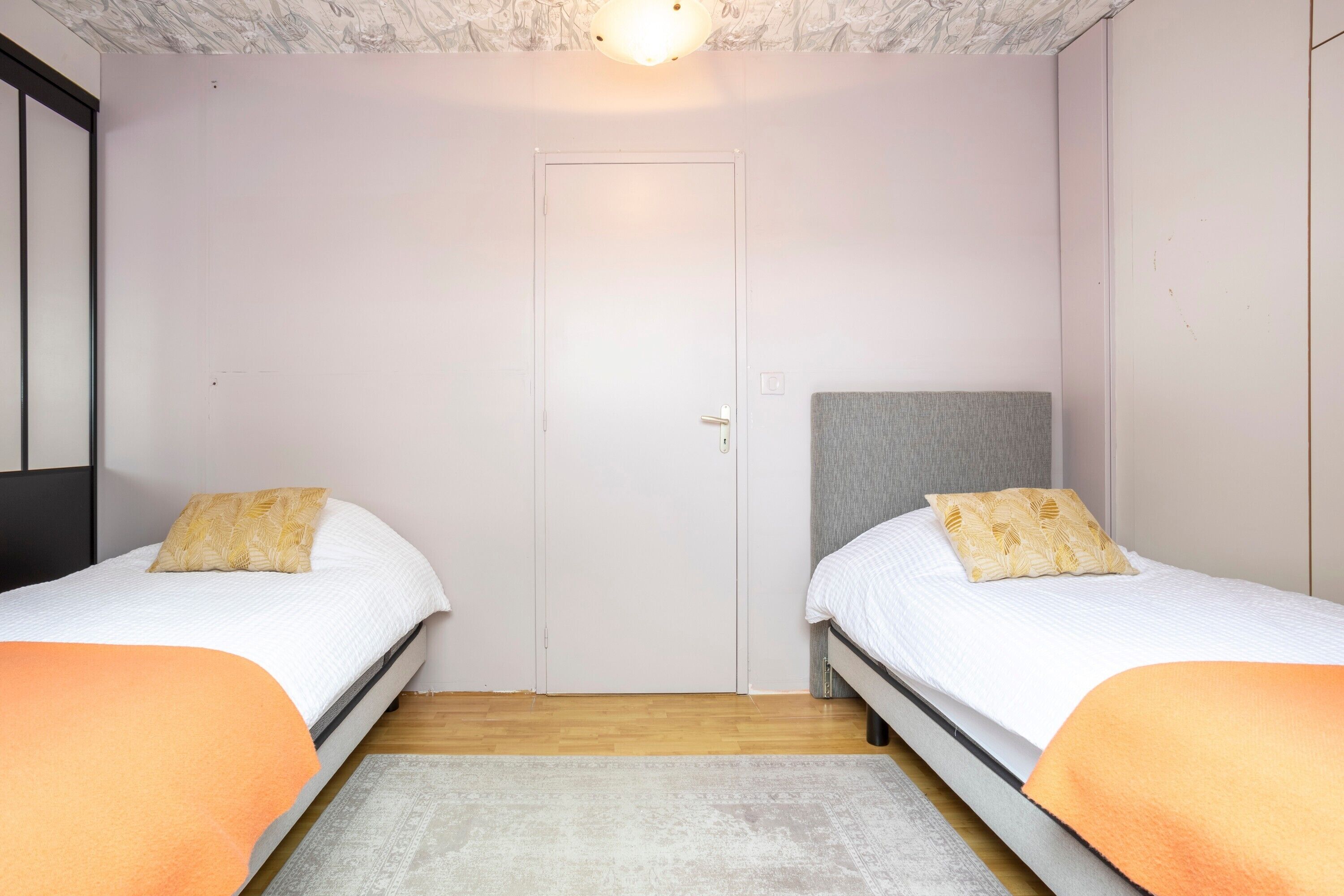 Een slaapkamer met twee eenpersoonsbedden, een deur en een lamp aan het plafond.