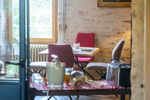 Een eetruimte met een tafel voor twee personen, een rode stoel en een raam met uitzicht op groen.