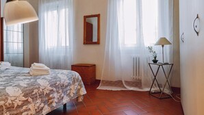 A bedroom with a bed, a bedside table with a lamp, a mirror, and a window with sheer curtains. - Apartment 'Borgo Pinti 49' with Private Terrace, Wi-Fi and Air Conditioning (Florence)