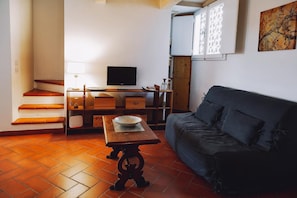 Un salon avec un canapé, un téléviseur, une table sur laquelle se trouve un saladier, une lampe et un escalier.