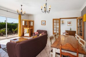 A spacious living area with a large wooden dining table, a brown sofa, and a chandelier. - Holiday Home 'Breeze - Adults Only' with Sea View, Wi-Fi and Air Conditioning (Albufeira)