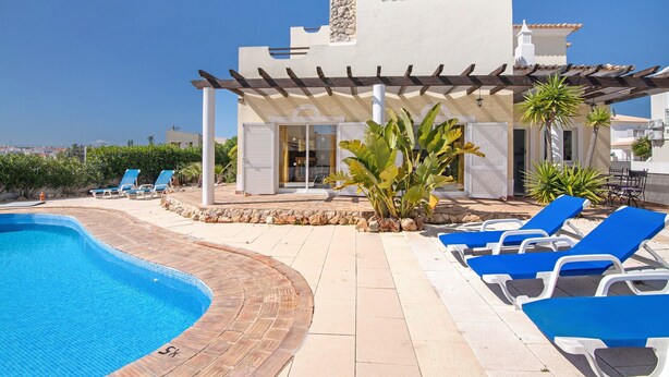 Un área junto a la piscina con sillones de descanso, una piscina y un edificio con chimenea de piedra.