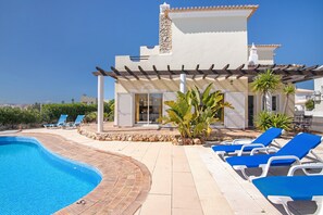 A poolside area with lounge chairs, a pool, and a building with a stone chimney. - Holiday Home 'Breeze - Adults Only' with Sea View, Wi-Fi and Air Conditioning (Albufeira)