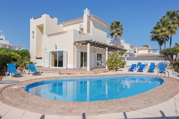 A poolside area with a pool, lounge chairs, and a building with a white facade and a stone accent wall. - Holiday Home 'Breeze - Adults Only' with Sea View, Wi-Fi and Air Conditioning (Albufeira)