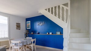 Ein Zimmer mit blauer Akzentwand, einer weißen Treppe, einem Esstisch mit Stühlen und einem Heizkörper.