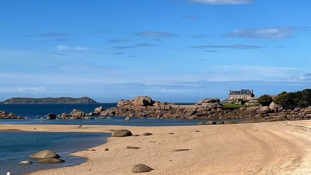 Eine Küstenlandschaft mit Sandstrand, großen Felsen und einem Haus mit geneigtem Dach.