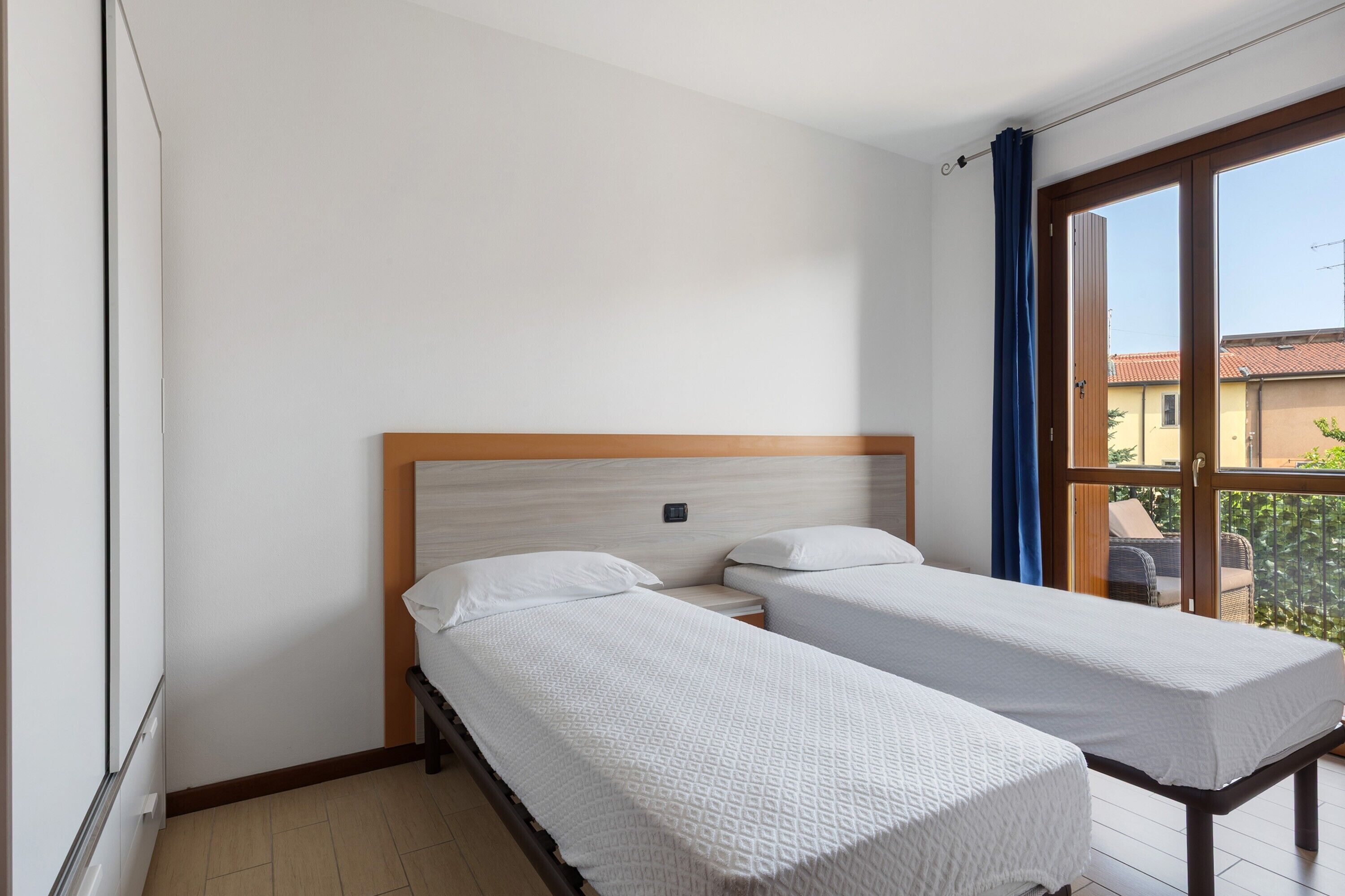 Ein Zimmer mit zwei Einzelbetten, einem Holzkopfstück, einem Fenster mit Blick und einem Balkon.