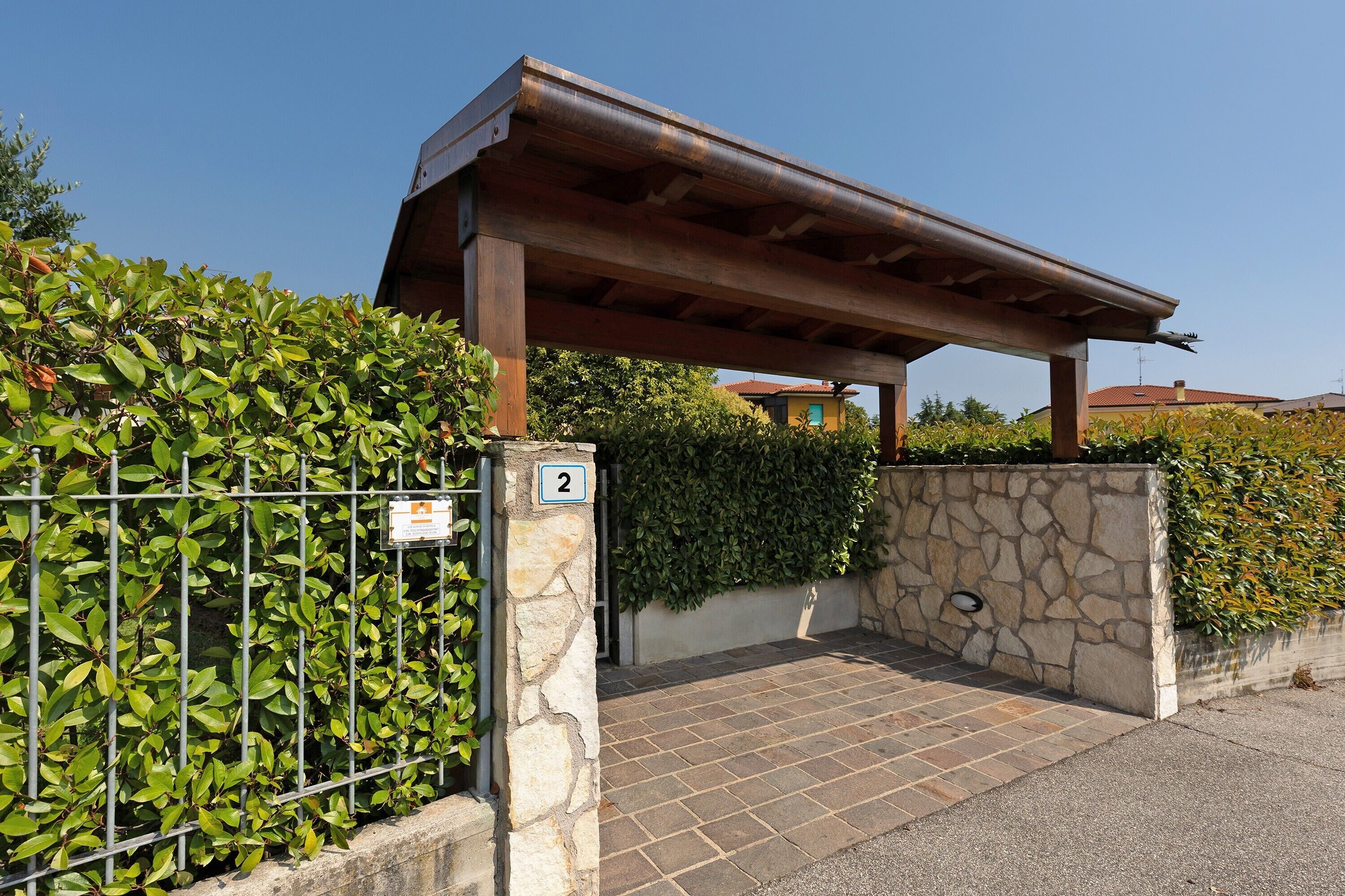Ein begrenzter Eingang mit einer Steinmauer, einem Metallzaun und einer Pergola.
