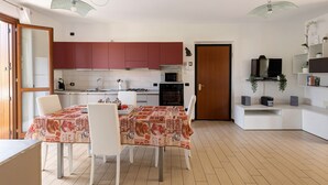 Een moderne keuken met rode kastjes, een eettafel met een tafelkleed met koffiethema, witte stoelen en een televisie op een wit plank.