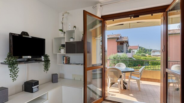 Een balkon met een tafel en stoelen, een televisie op een plank en een schuifdeur naar buiten.