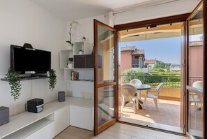 A balcony with a table and chairs, a television on a shelf, and a sliding glass door leading to the outside. - Holiday Home 'Casa Vacanze Da Ricky' with Shared Pool, Wi-Fi and Air Conditioning (Peschiera)