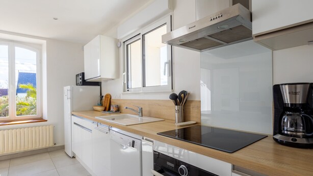 A modern kitchen with white cabinets, a dishwasher, a stove, a coffee maker, and a window with a view of greenery.