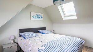 A bedroom with a bed, a nightstand, a lamp, a ceiling light, a window, and a wall art piece.