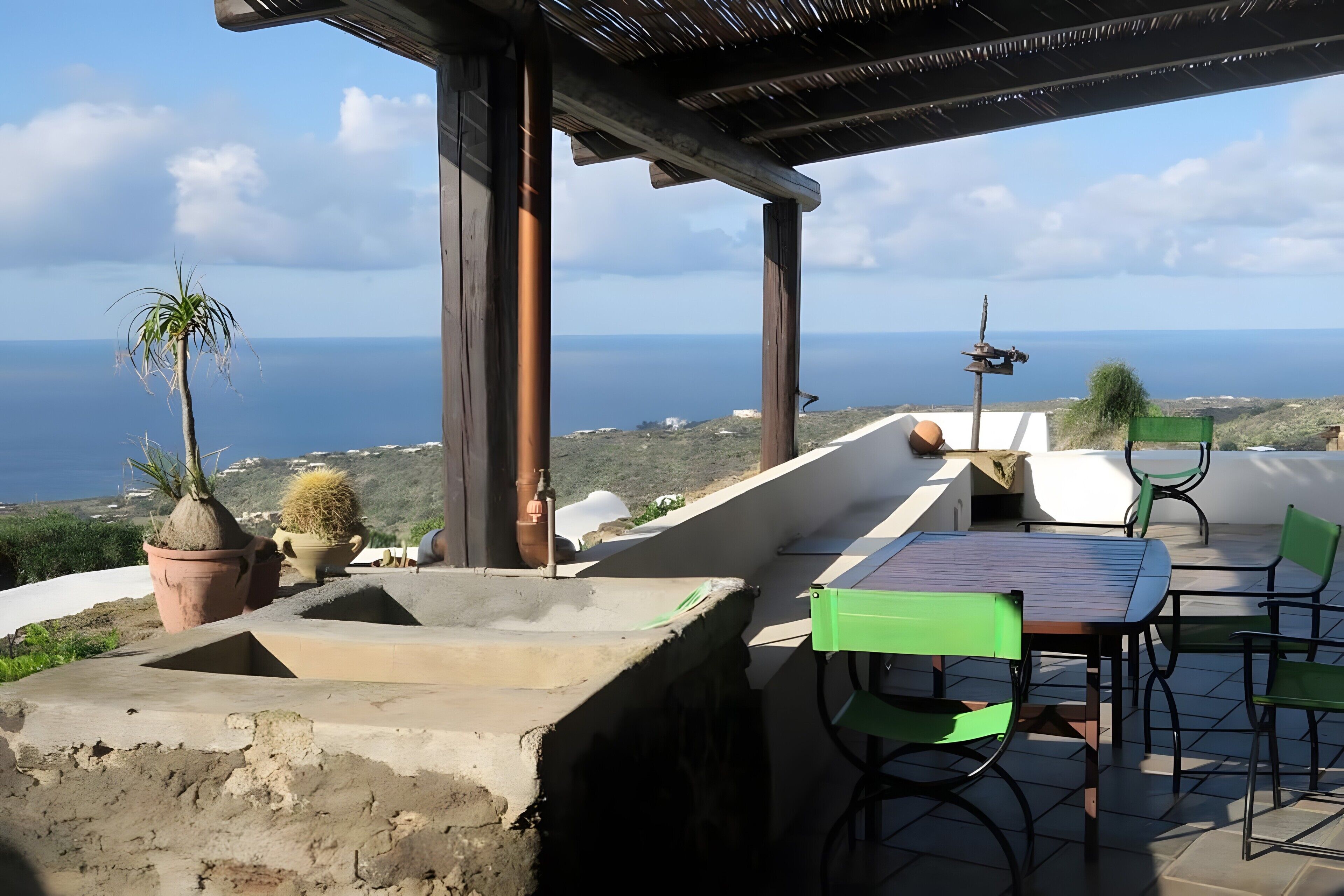 Une terrasse extérieure avec une table et des chaises, une vue sur la mer et des plantes en pot.