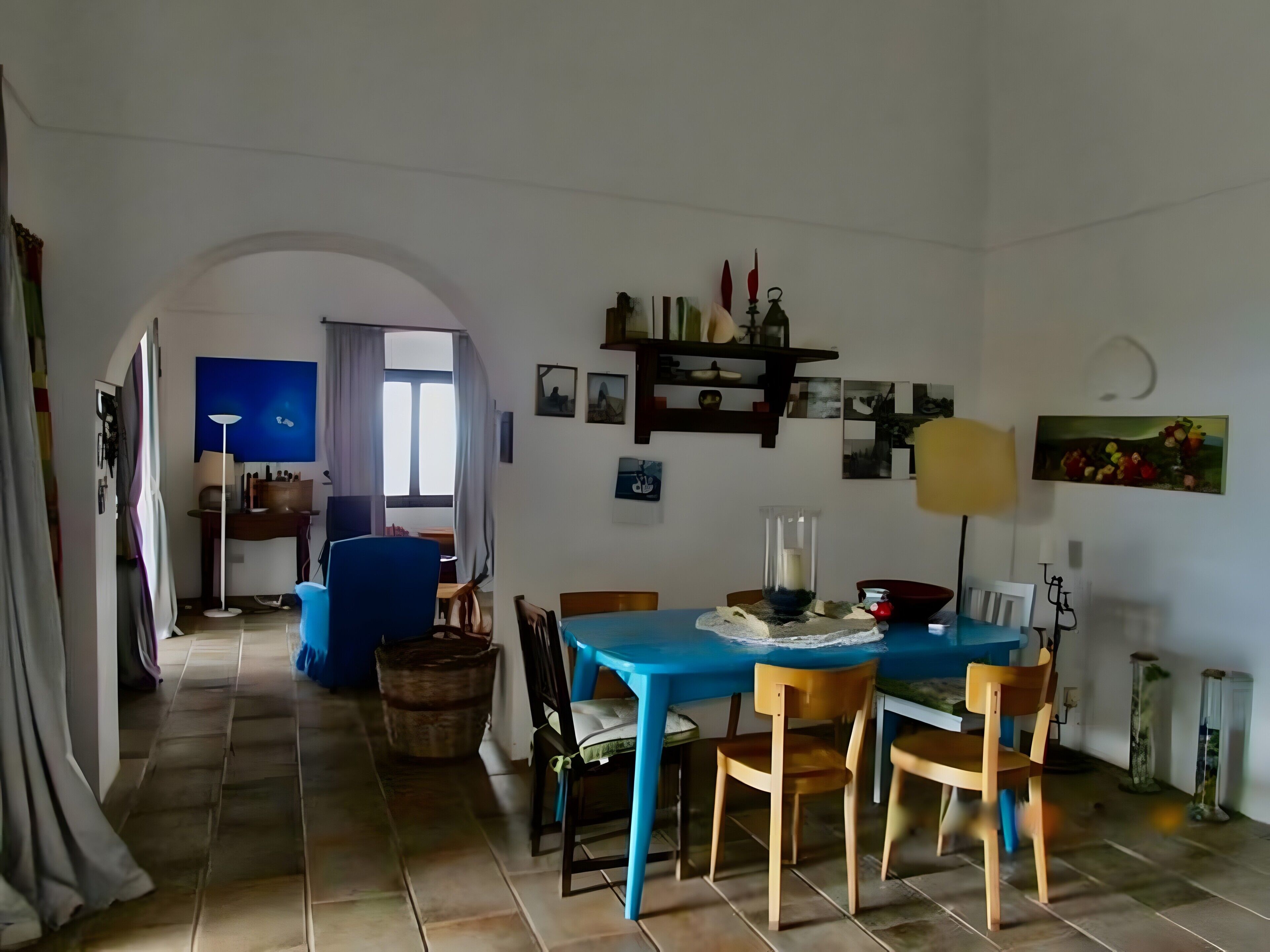 Ein Essbereich mit blauem Tisch, Holzstühlen, einer Chandelüster und Blick durch einen Bogen in einen anderen Raum.