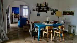 Comedor con una mesa azul, sillas de madera, una araña y vista a otra habitación por un arco.