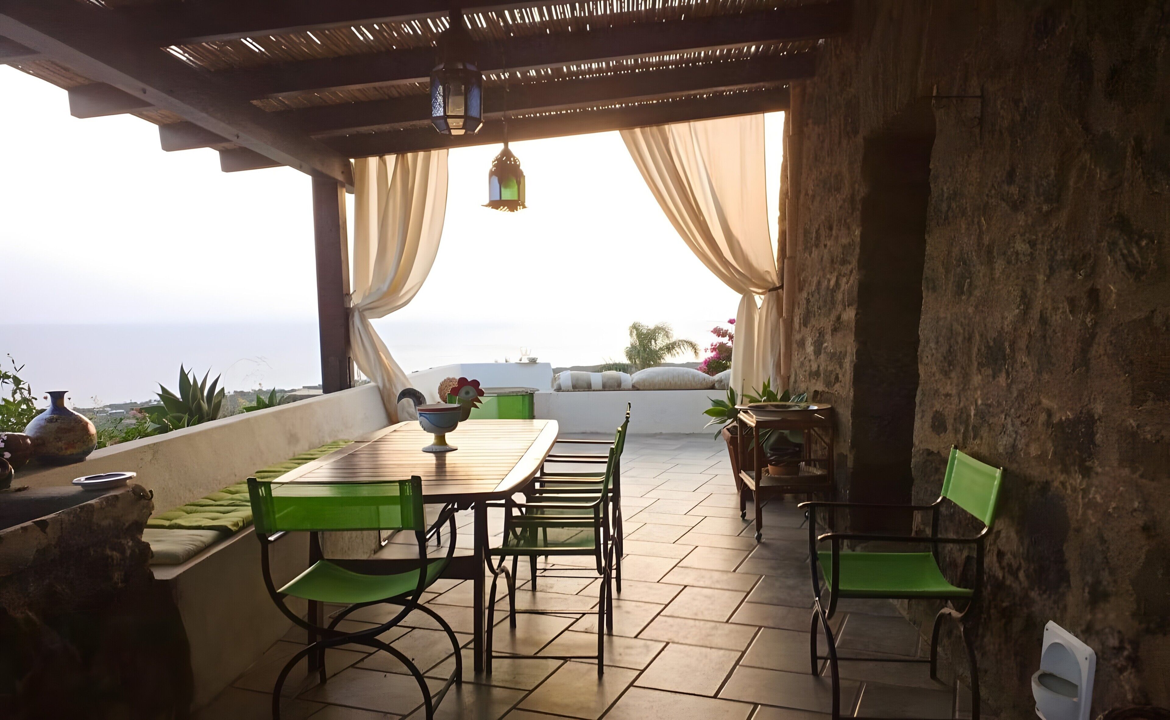 Une terrasse extérieure avec une table et des chaises, une lanterne suspendue et une vue sur la mer.