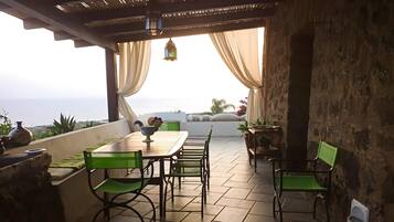 Une terrasse extérieure avec une table et des chaises, une lanterne suspendue et une vue sur la mer.