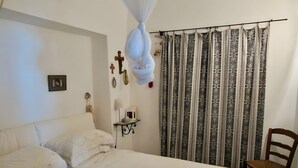Un dormitorio con cama, una silla, una mesita de noche con lámpara y una cortina estampada.