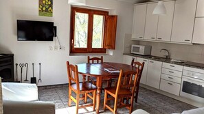 Un comedor con mesa y sillas de madera, una ventana con contraventanas de madera, un microondas y armarios en una cocina.