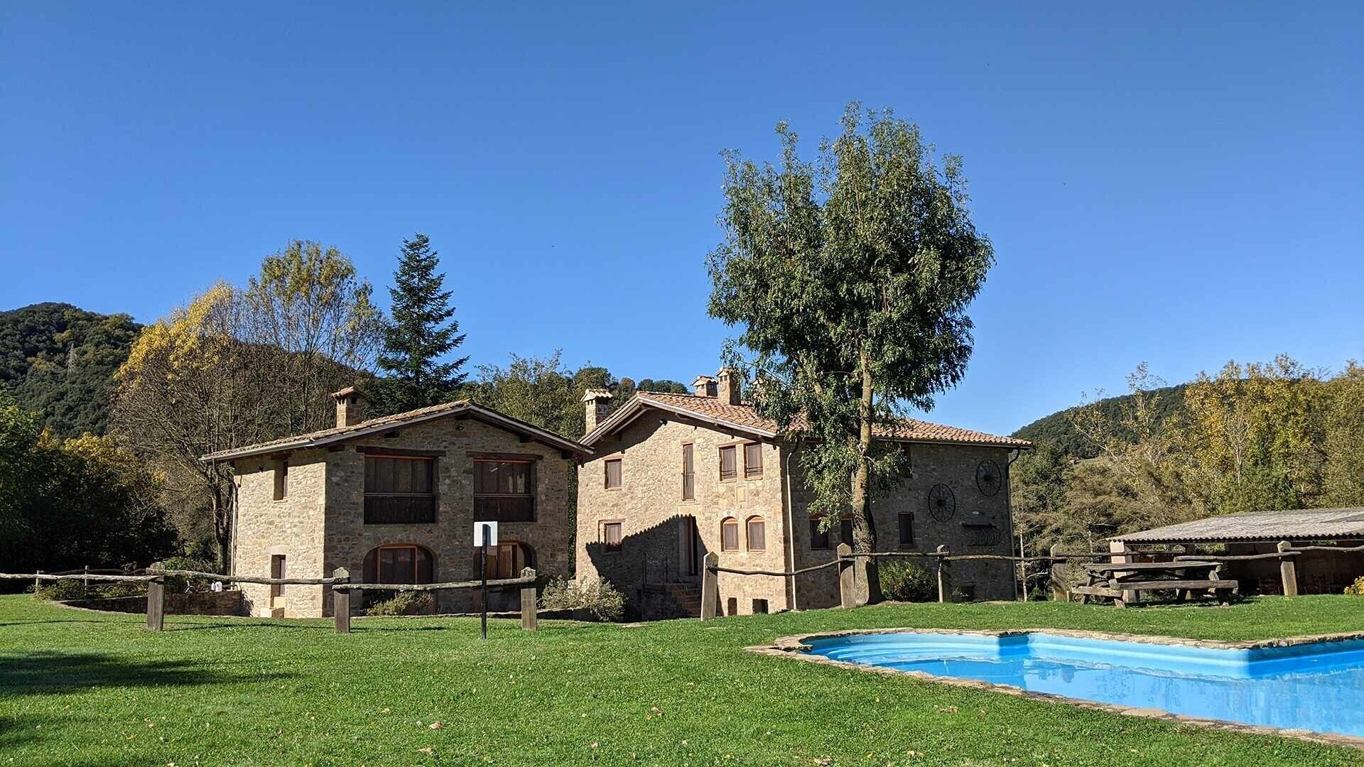 Un edificio de piedra con piscina, rodeado de césped y árboles.