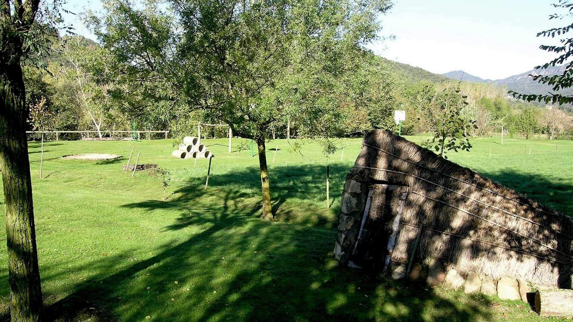Un campo cubierto de césped con árboles, un muro de piedra y una valla.