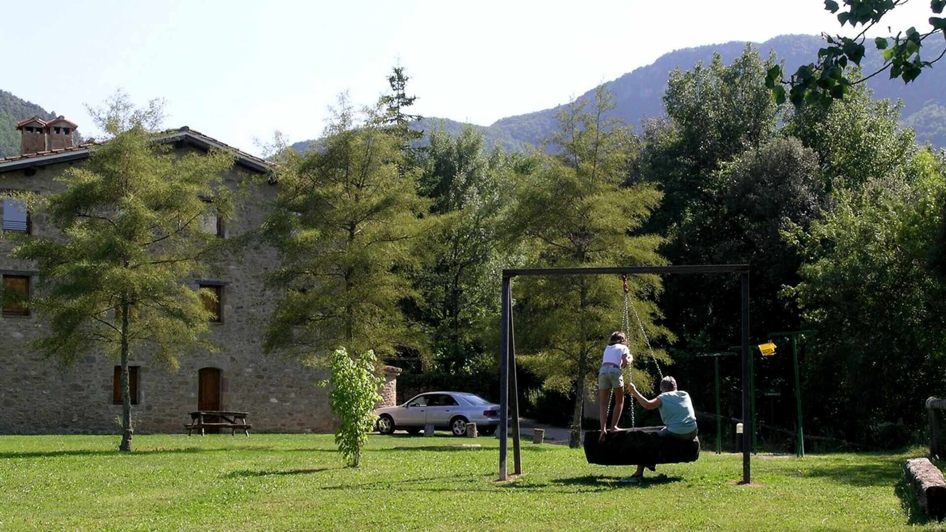 A park with a swing set, a stone building, and a car parked nearby.