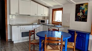 Une cuisine avec des meubles blancs, une table bleue et un tableau représentant un cheval.