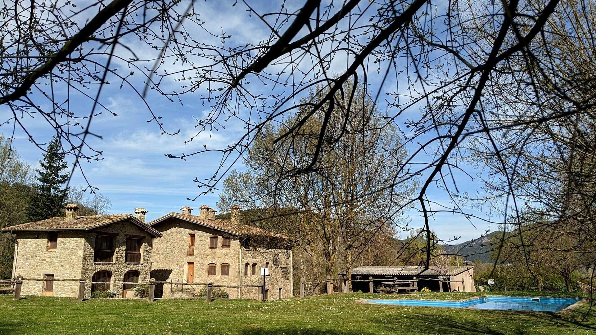 Ein Gebäude aus Stein mit einem Pool, umgeben von Bäumen und einem klaren Himmel.