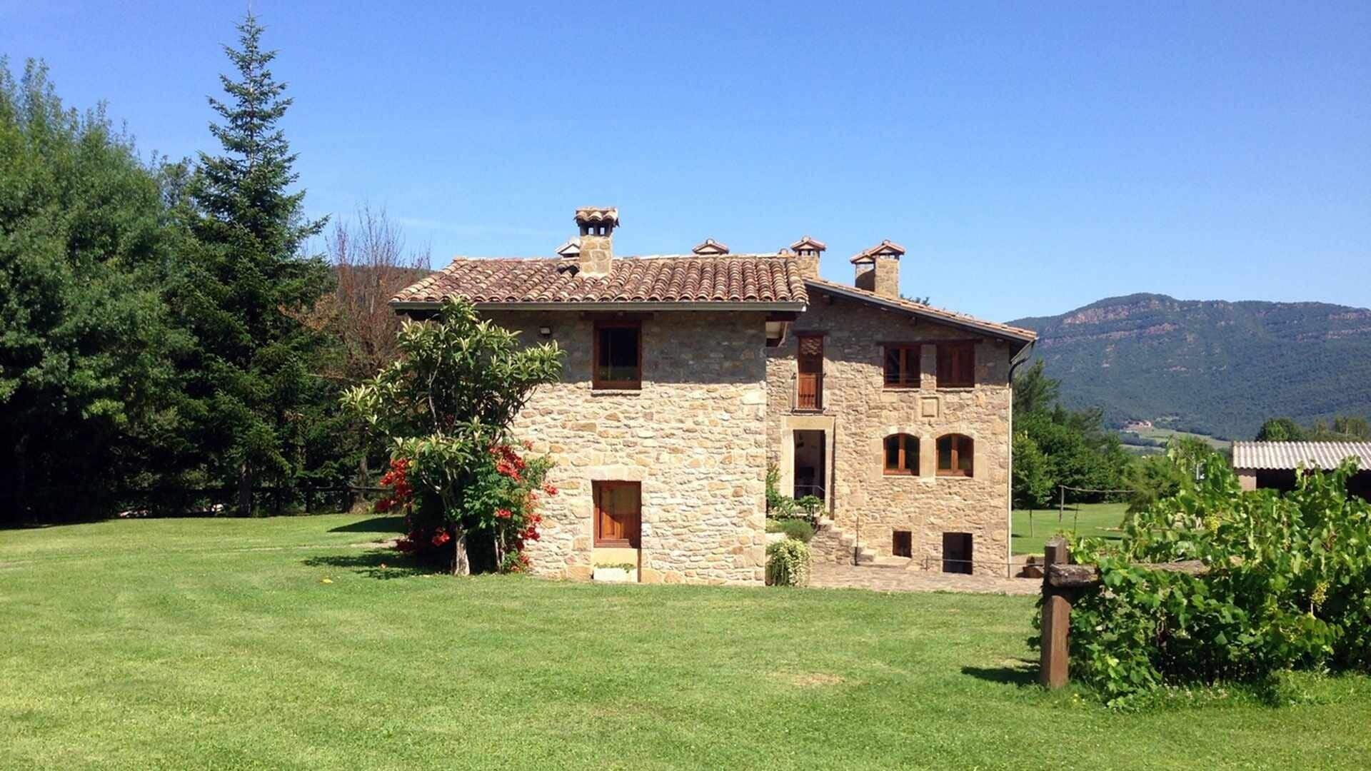 Un edificio de piedra con techo de tejas, rodeado de un campo cubierto de hierba y árboles.