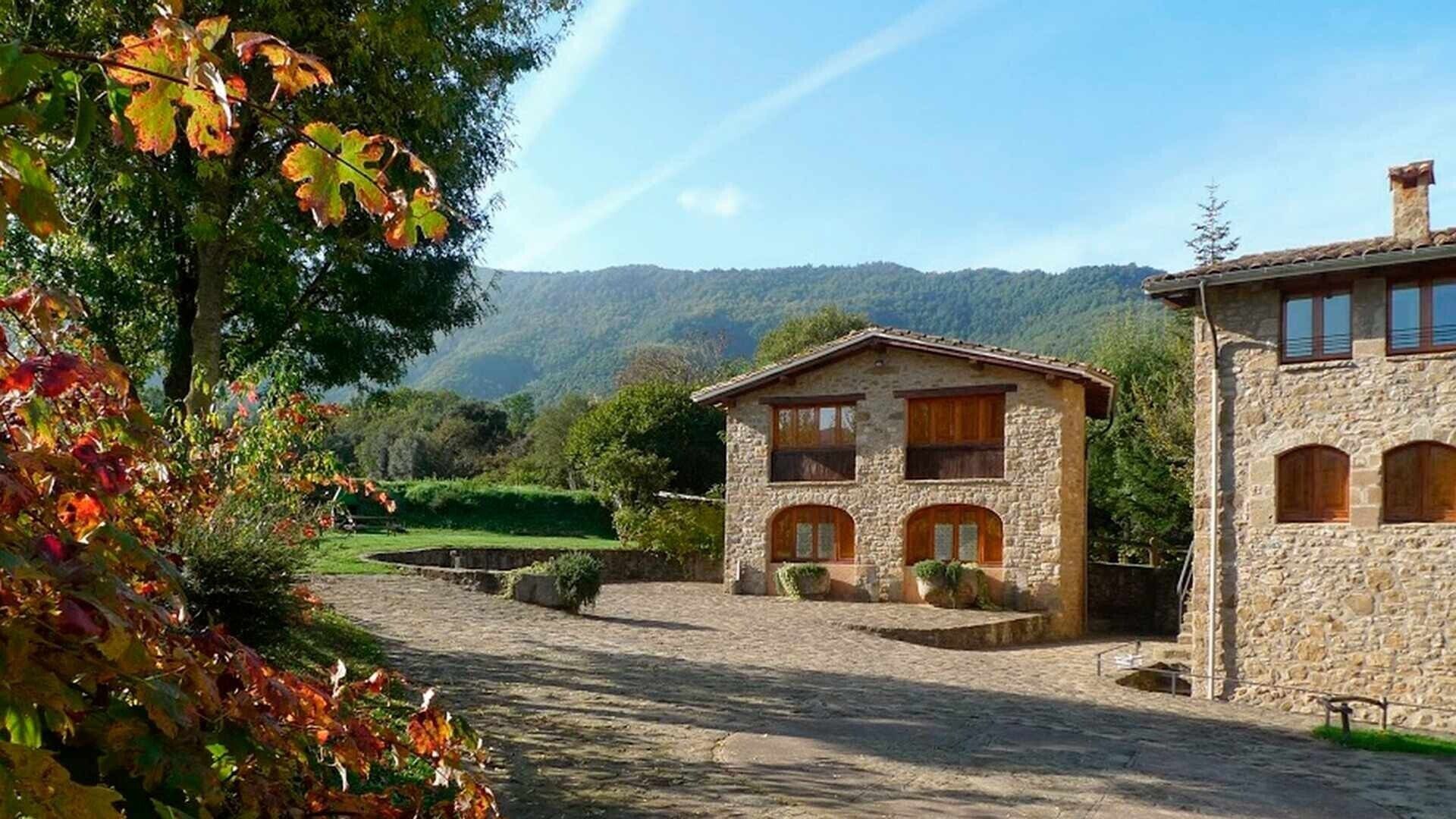 Un edificio de piedra con un sendero de piedras que lo conduce, rodeado de árboles y colinas.