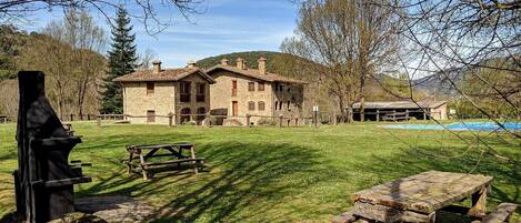 A stone building with a large lawn, picnic tables, and a swimming pool.
