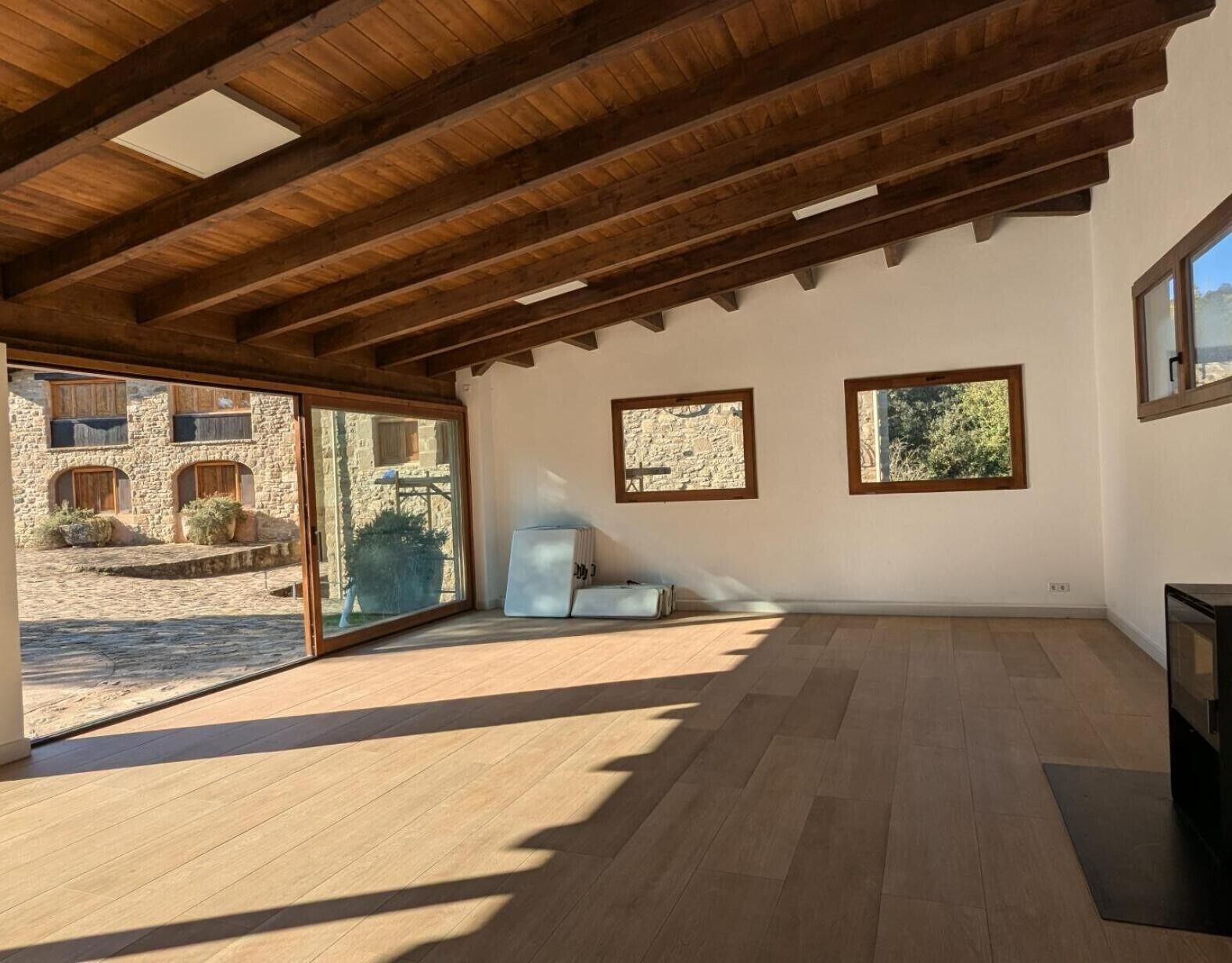 Una habitación amplia con vigas de madera, ventanas grandes y vistas a un edificio de piedra.