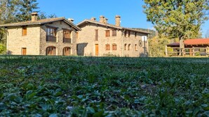 A stone building with multiple windows and a chimney, surrounded by grass and trees.