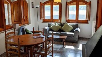 Een eethoek met houten stoelen, een ronde tafel en een grijze bank met groene kussens.
