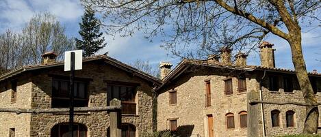 A stone building with multiple windows and a chimney, surrounded by grass and trees.