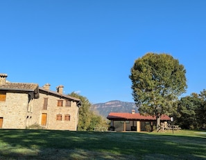 A stone building with a red-tiled roof, a large tree, and a mountain in the background.