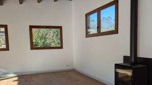 A room with a fireplace, wooden flooring, and three windows with wooden frames.