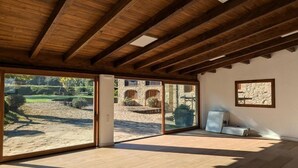 A spacious room with a high ceiling, large sliding glass doors leading to an outdoor area, and a stone wall with a window.