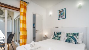 Ein Hotelzimmer mit einem Bett, zwei Kissen, einem Nachttisch, einer Lampe, einem Stuhl, einem Fenster mit Vorhängen und einer Tür.