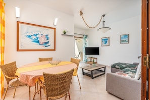 A living room with a dining table, wicker chairs, a sofa, a TV, and artwork on the walls.