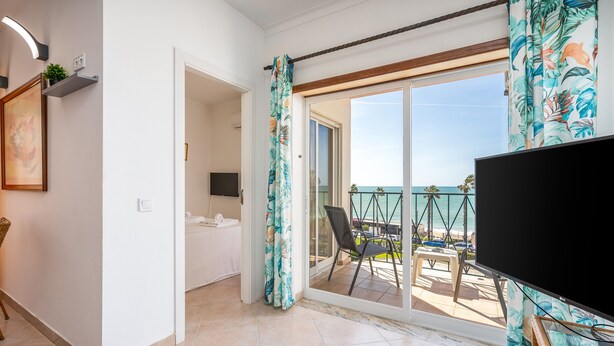 Ein Zimmer mit Fernseher, Bett, Balkon mit Meerblick und Stuhl.