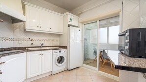Eine Küche mit weißen Schränken, einer Waschmaschine, einem Kühlschrank und einer Mikrowelle.