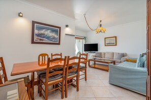 Ein Wohnzimmer mit einer Couch, Fernseher, einem Holzessttisch, Stühlen und einem Gemälde an der Wand.