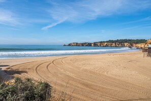 A sandy beach with tire tracks, a wooden structure, and cliffs in the background.