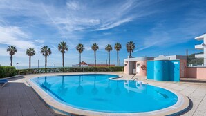Ein Pool mit geschwungener Kante, umgeben von Palmen und blauem Himmel.