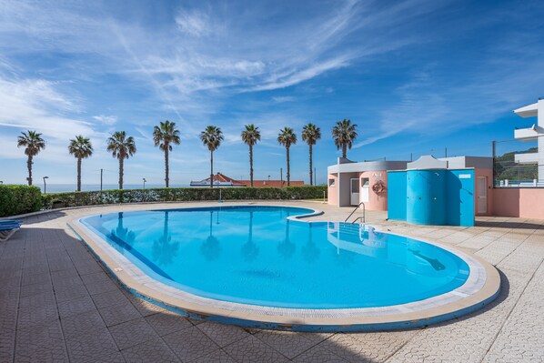 A swimming pool with a curved edge, surrounded by palm trees and a clear blue sky.