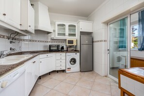 Eine Küche mit weißen Schränken, einer Mikrowelle, einem Kühlschrank, einer Waschmaschine und einem Spülbecken.