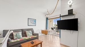 Un salon comprenant un canapé, une table basse, un téléviseur fixé au mur et un coin repas avec une table et des chaises.