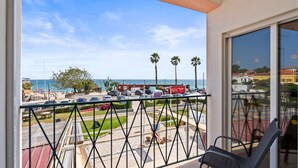 Un balcon avec vue sur la mer, les palmiers et les voitures garées.
